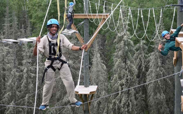 two students are suspended by ropes as they make their way through a ropes course on an outward bound course